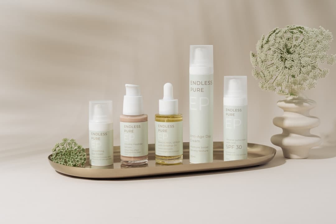 A beautifully arranged display of elegant skincare products on a marble tray against a soft, beige backdrop. The collection includes various bottles and jars, showcasing a range of serums, creams, and SPF protection. The minimalist design and soft pastel colors create a clean, luxurious aesthetic. A delicate floral arrangement in a textured vase adds a natural touch to the composition, enhancing the serene and sophisticated vibe.